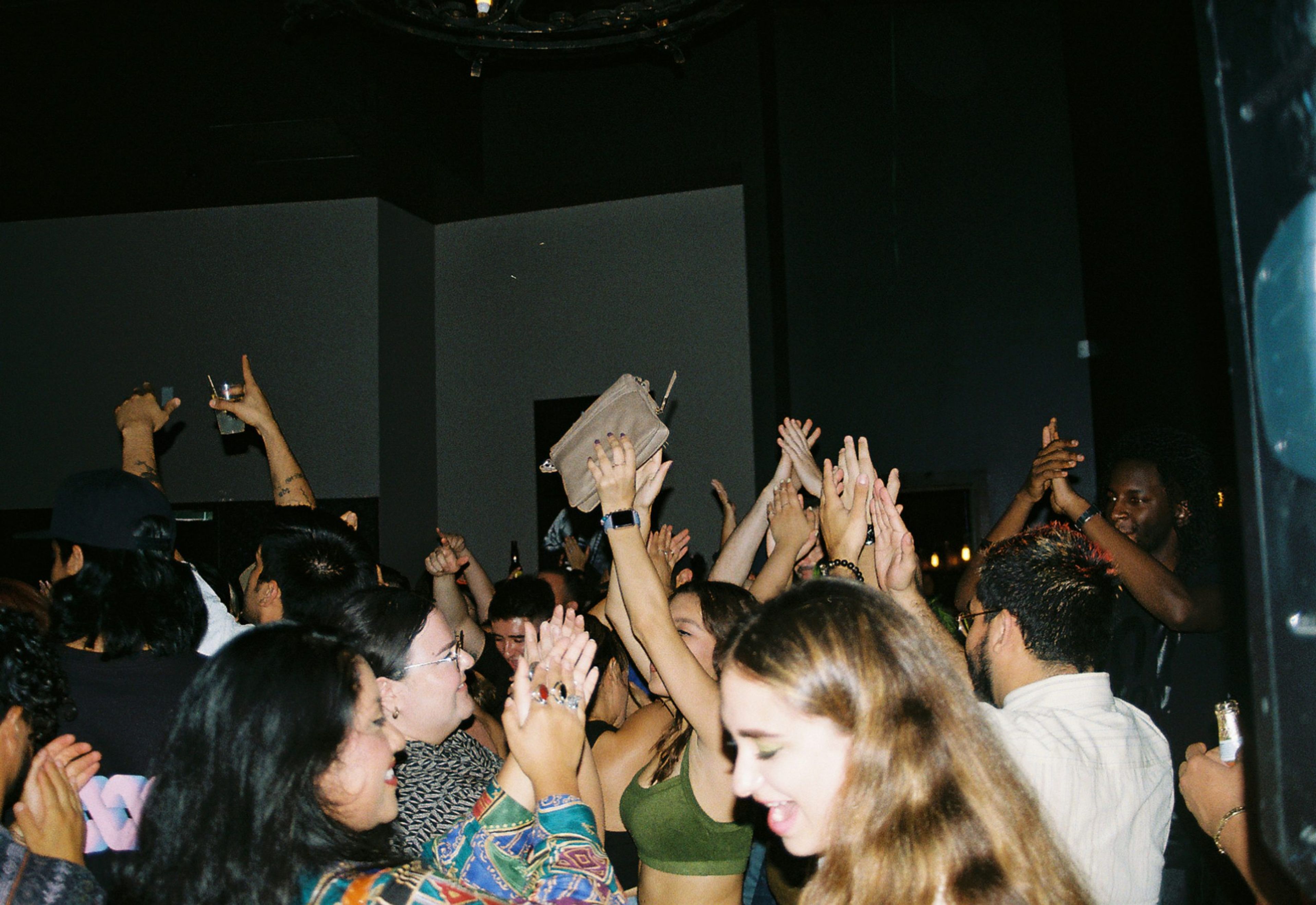 A lively crowd dancing and celebrating at a party with raised hands and drinks.