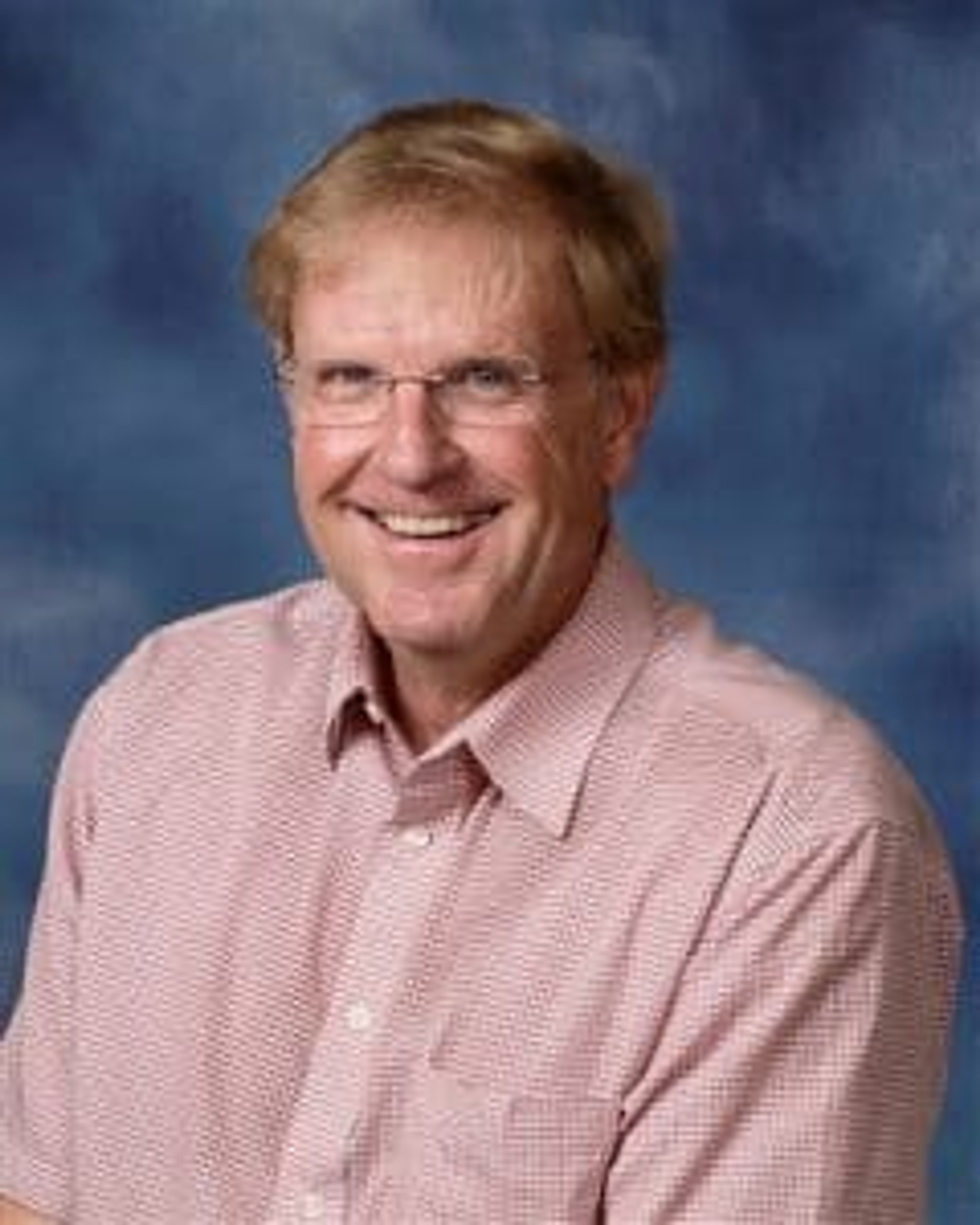 Smiling man with glasses wearing a checkered shirt against a blue background