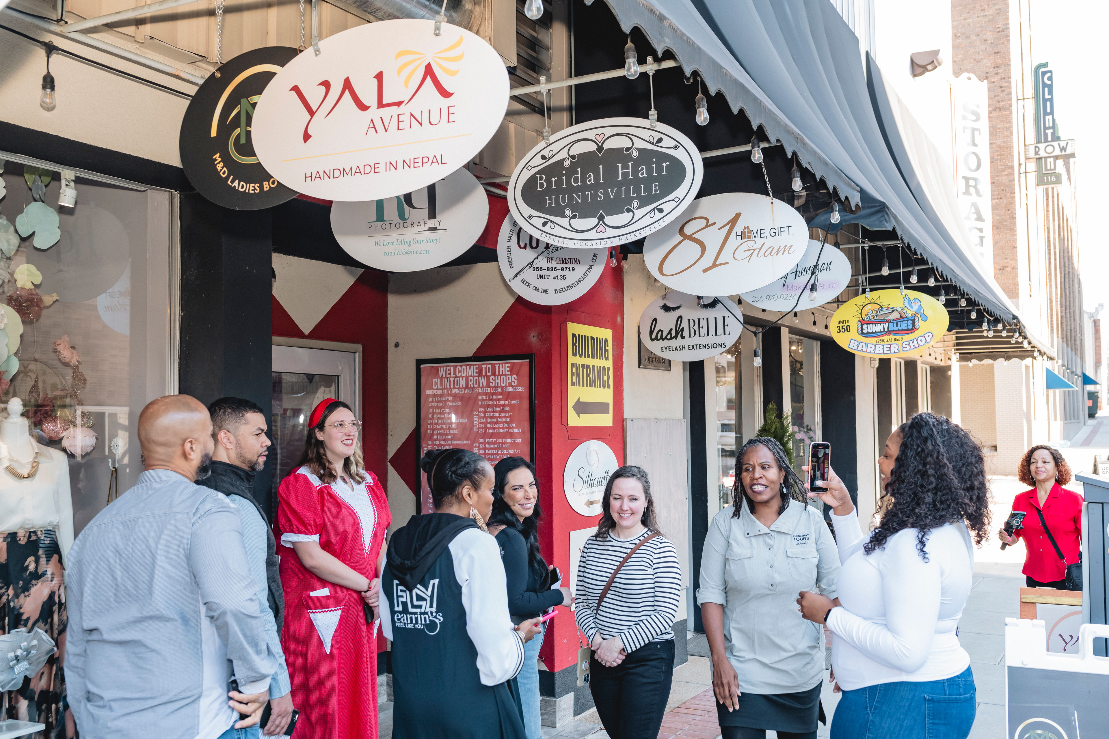 Group of people smiling and posing outside shops with various signs.