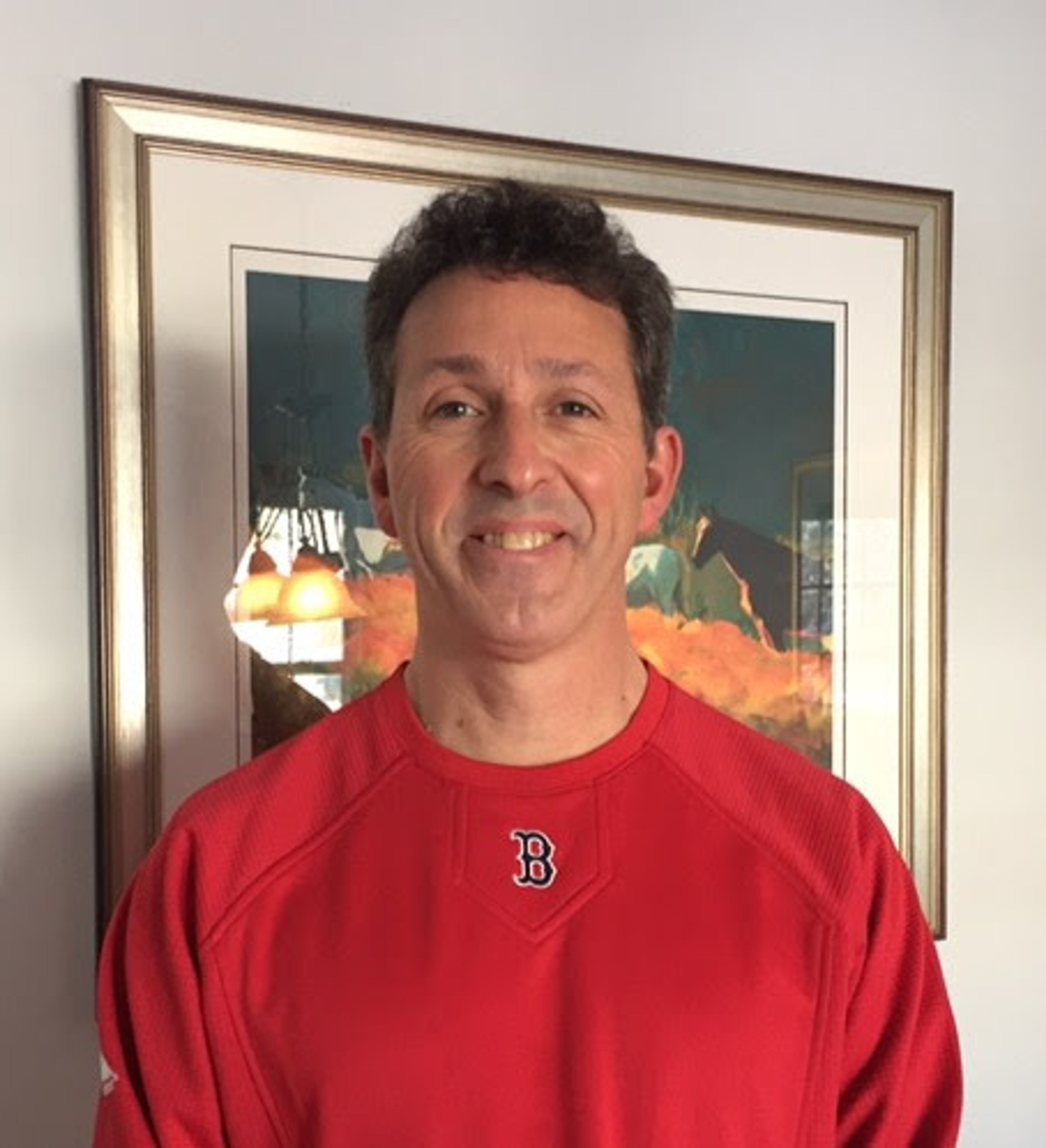 Smiling man in a red Boston shirt standing in front of a framed artwork.