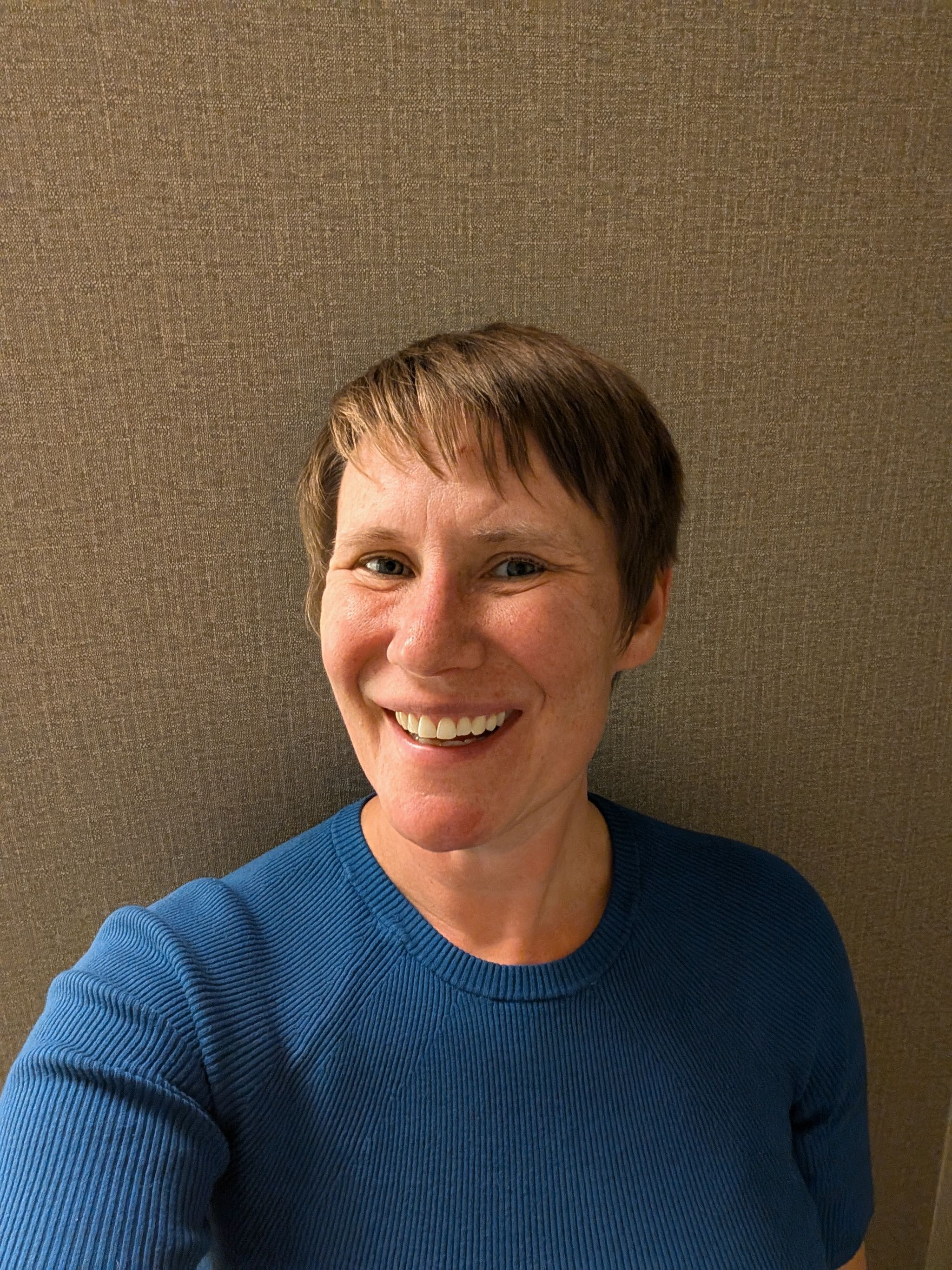 Person smiling in a blue shirt against a textured brown background