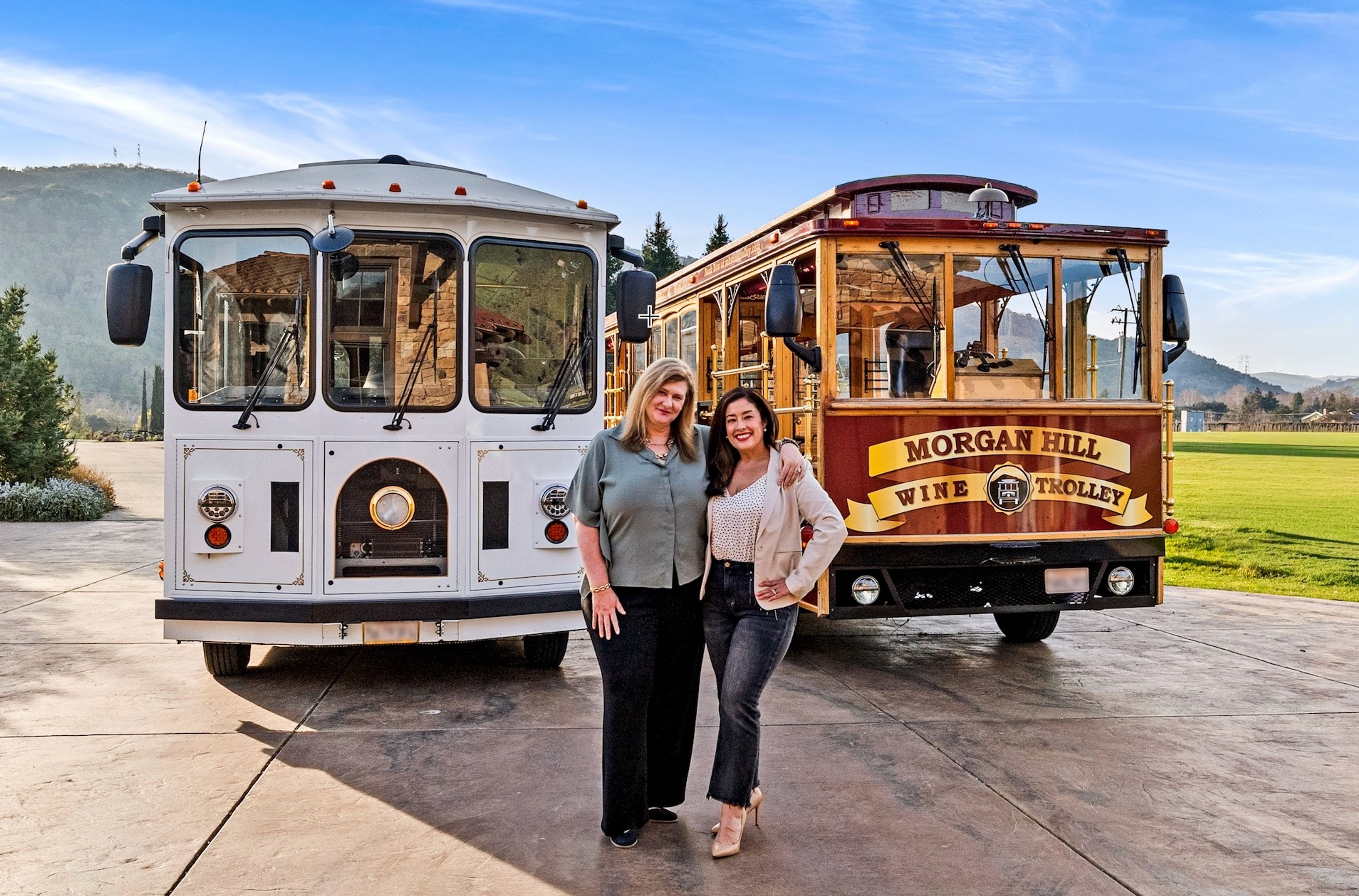 Two women pose in front of a white and a wooden wine trolley.