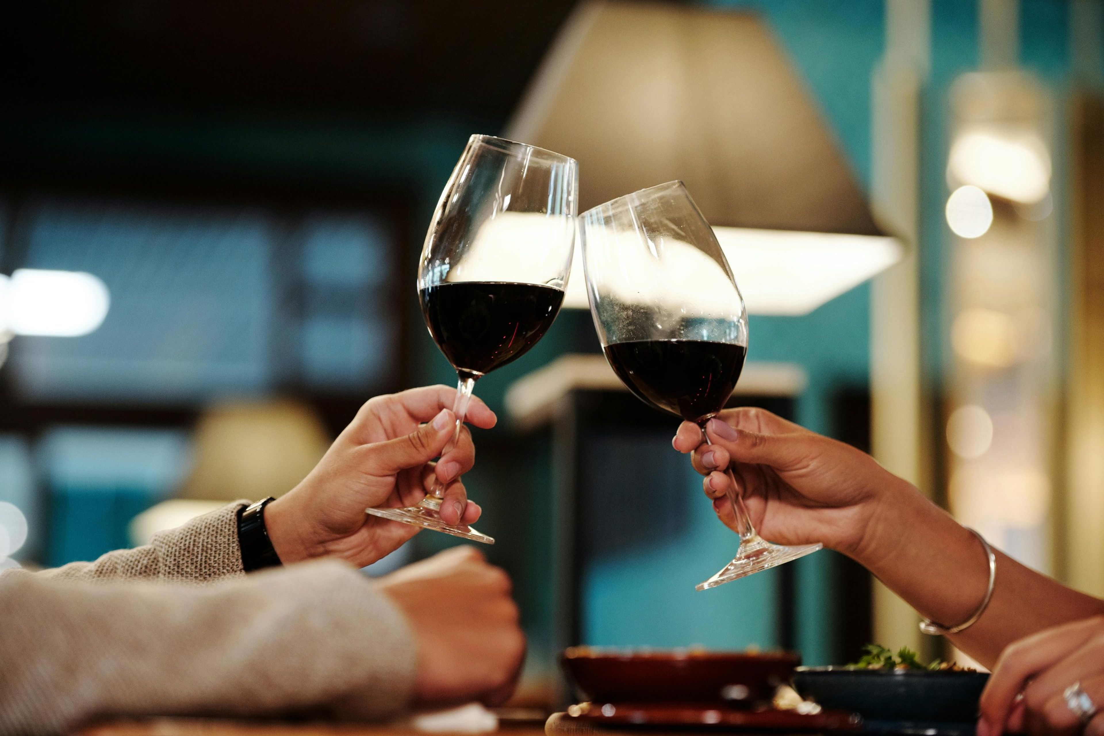 Two hands clinking wine glasses in a cozy restaurant setting