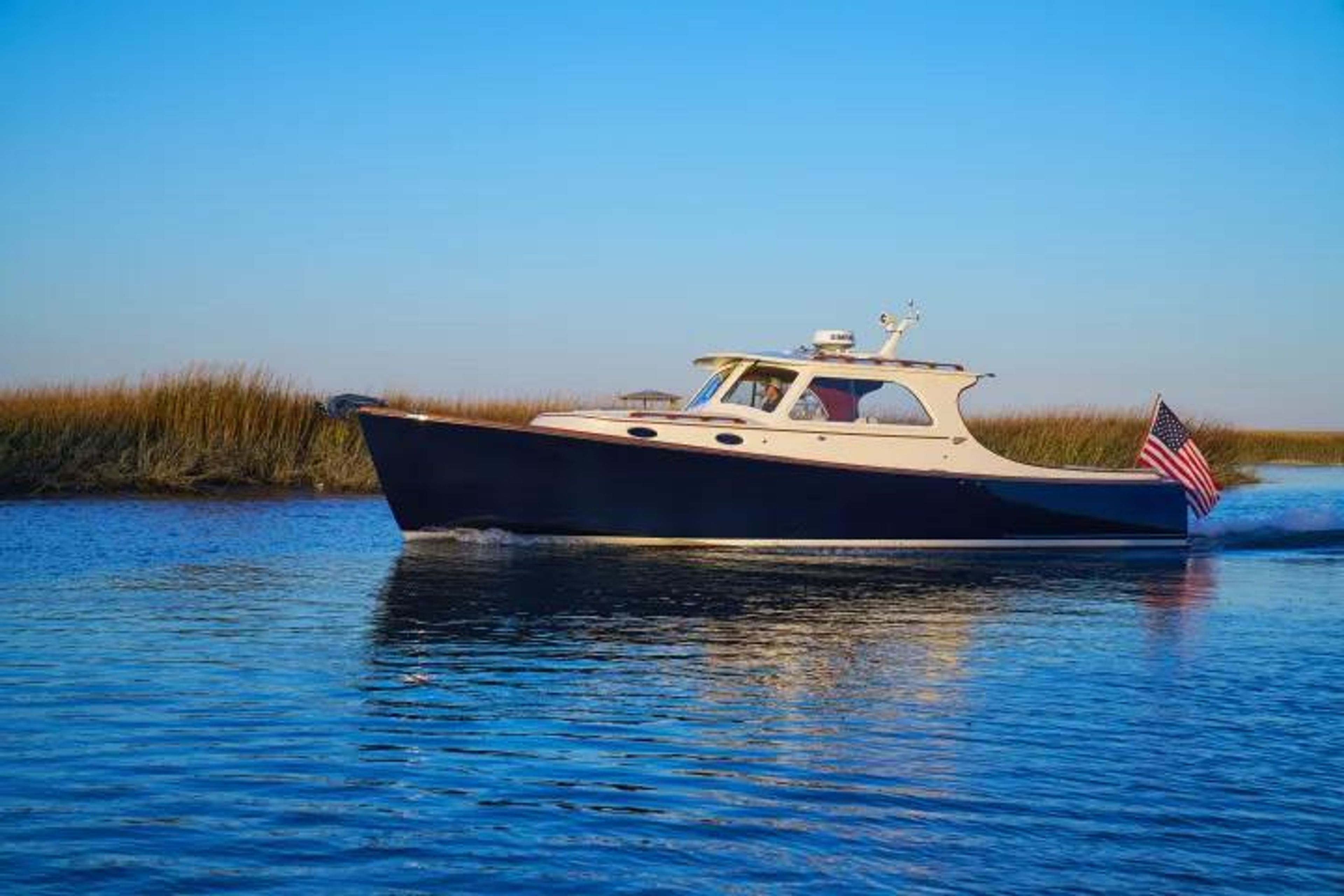 A boat with an American flag cruising on calm waters near marshland.