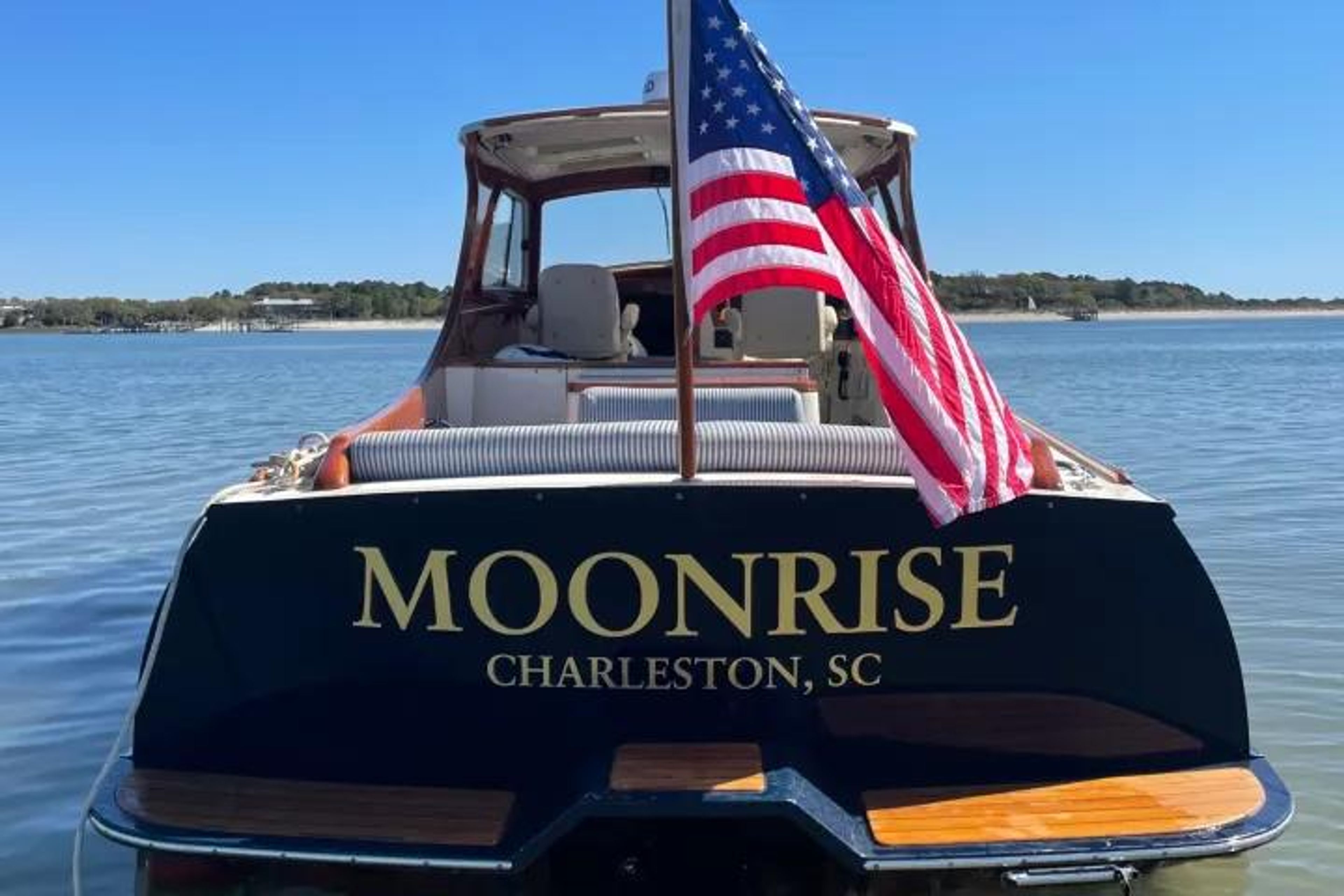 Back of a boat named Moonrise with an American flag on a calm water surface