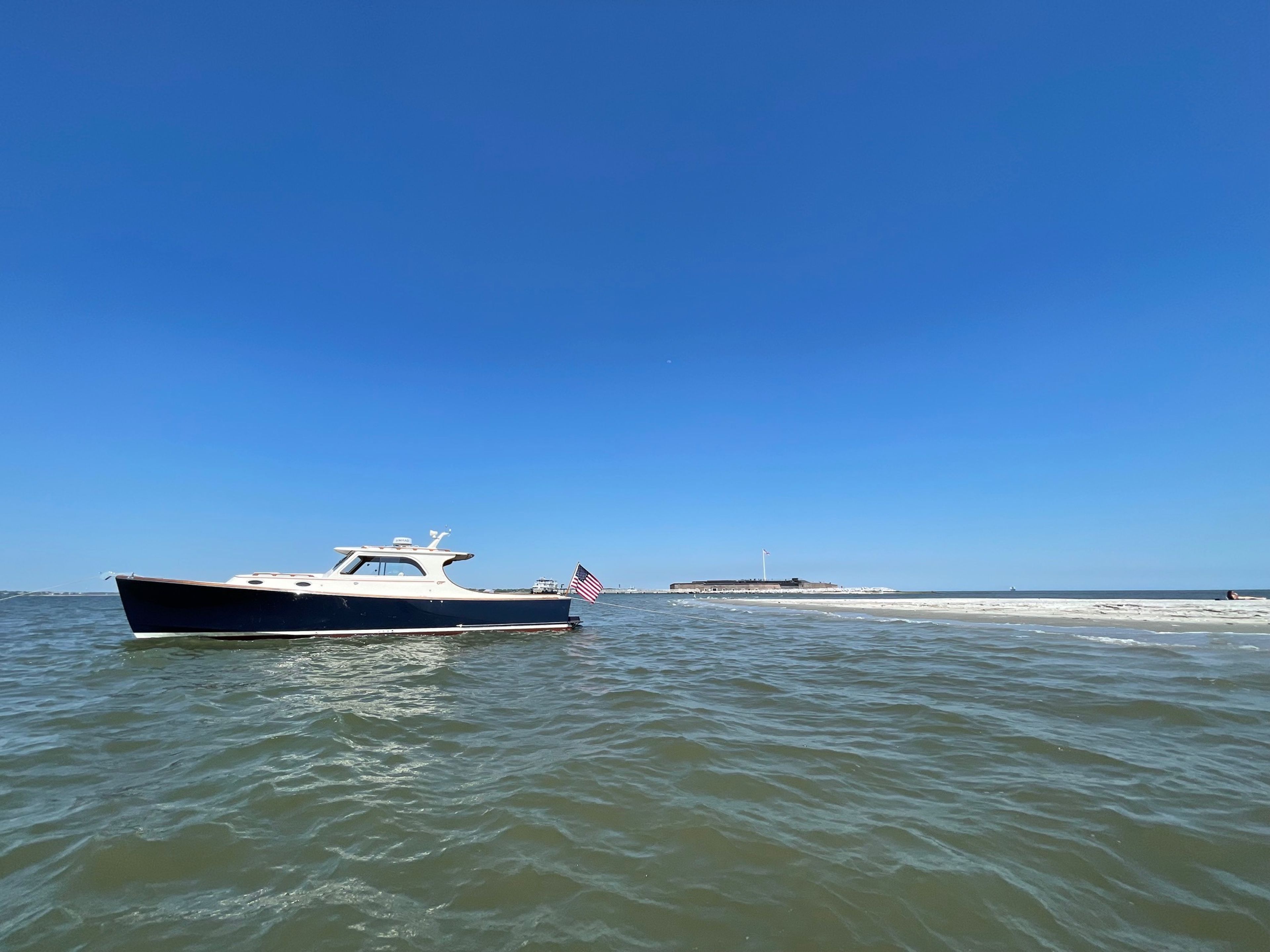 A boat with an American flag on calm waters under a clear blue sky.