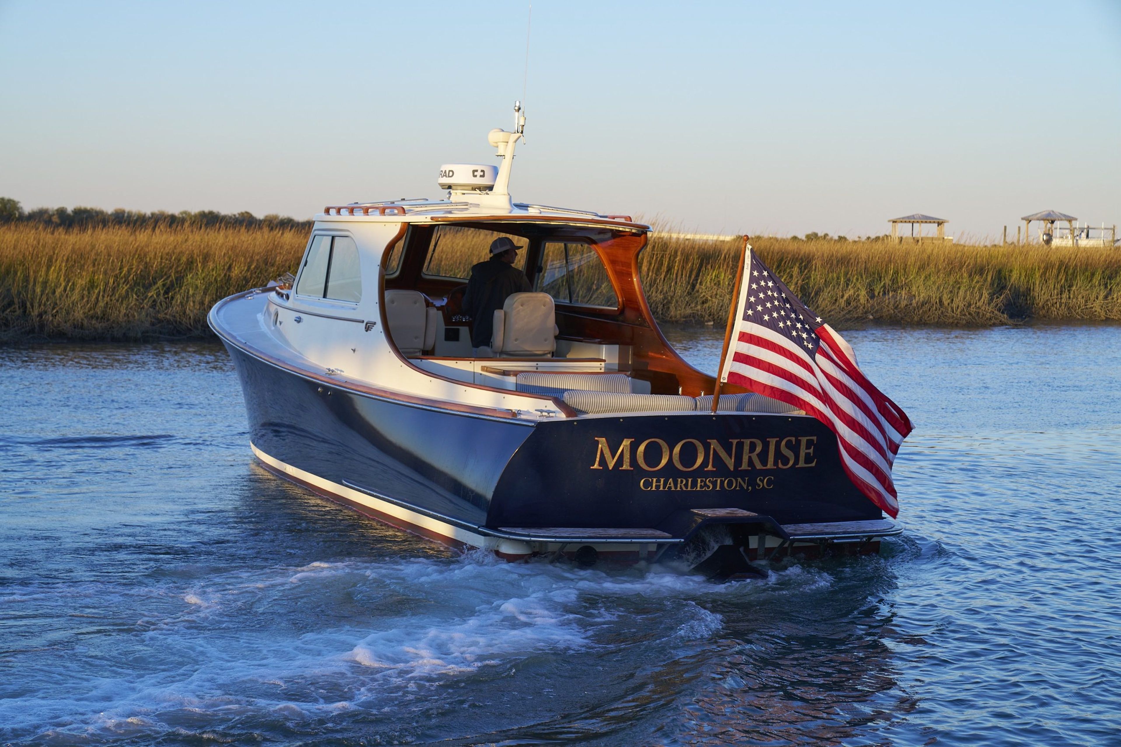 A boat named Moonrise with an American flag cruising in a marshy area.