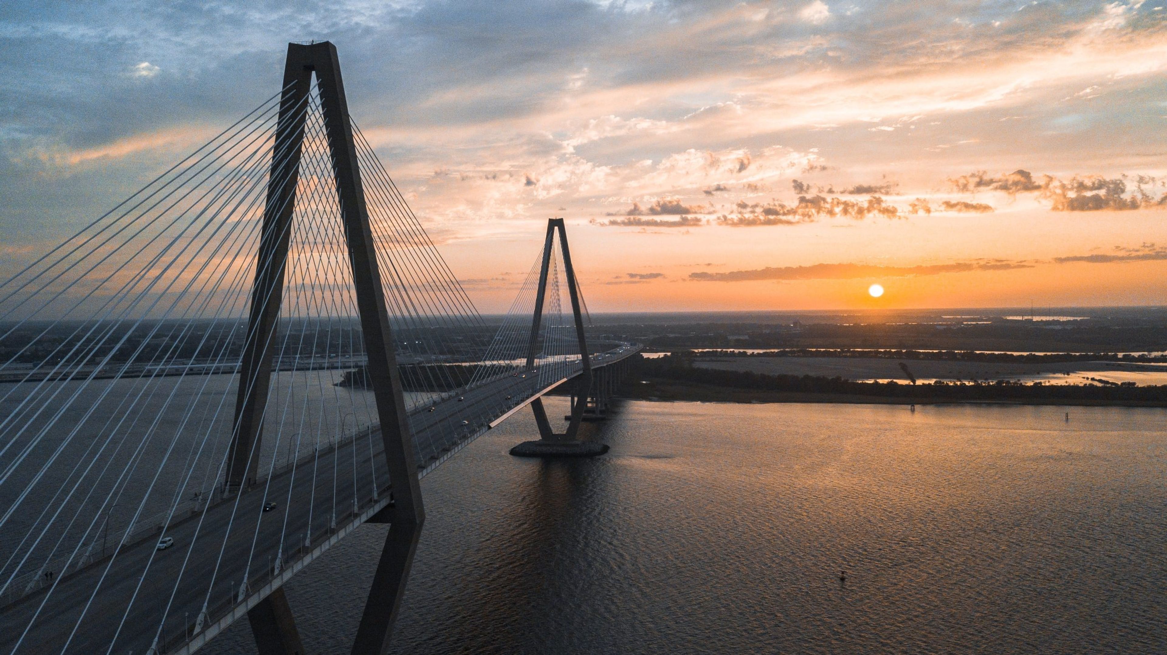 A cable-stayed bridge at sunset over a river with a colorful sky.