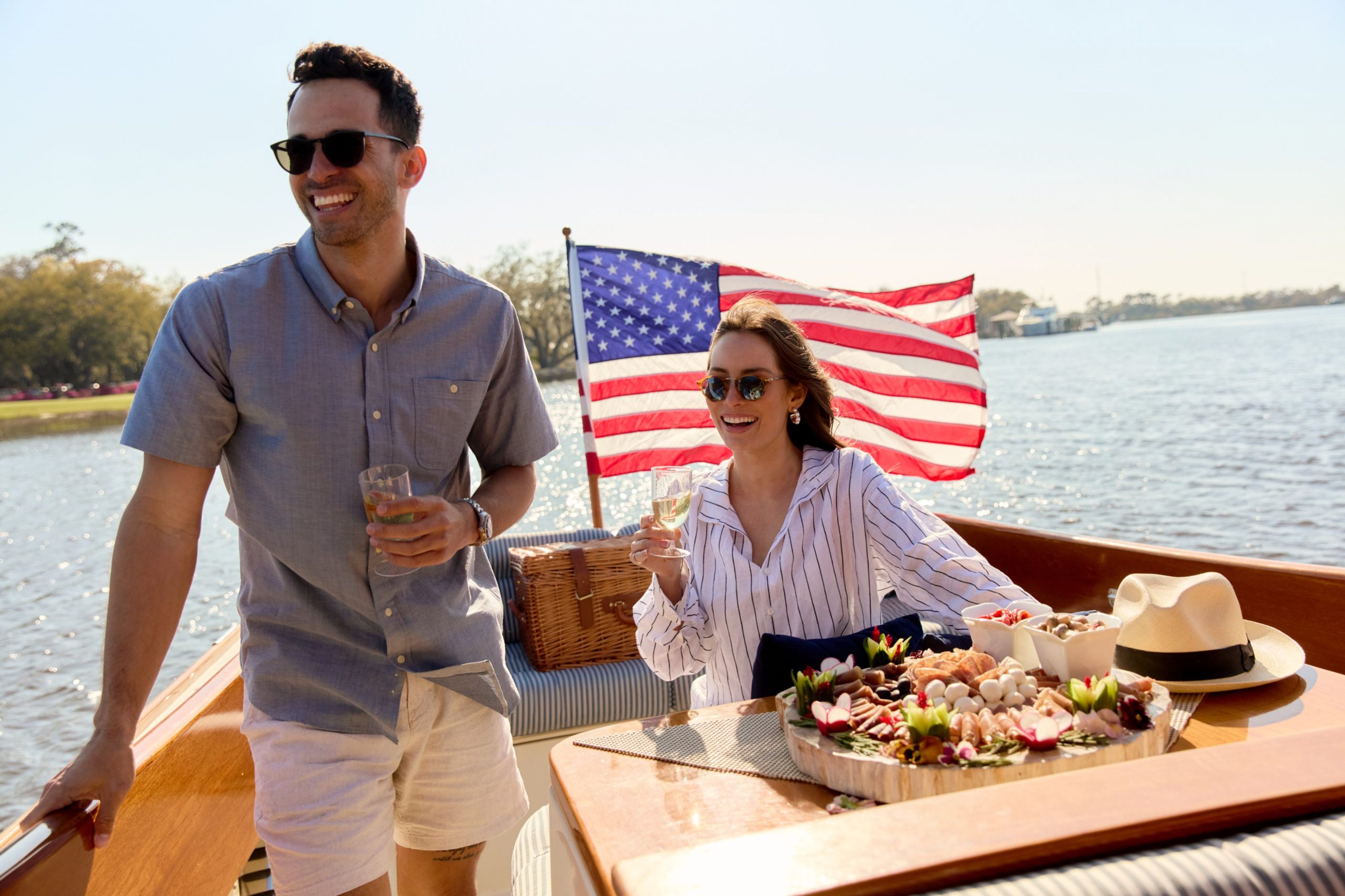 Couple enjoying drinks on a boat with a platter of food and an American flag in the background.