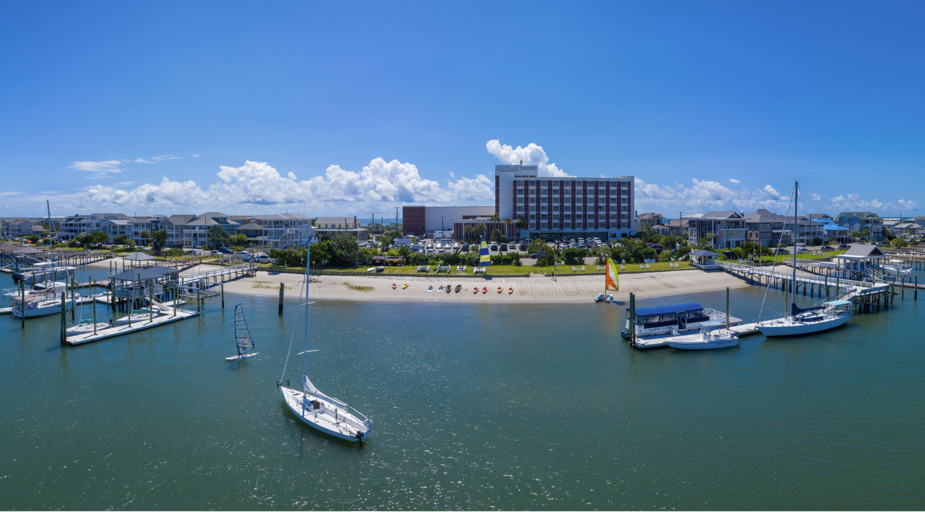 A marina with sailboats, a sandy beach, and a hotel under a clear blue sky.