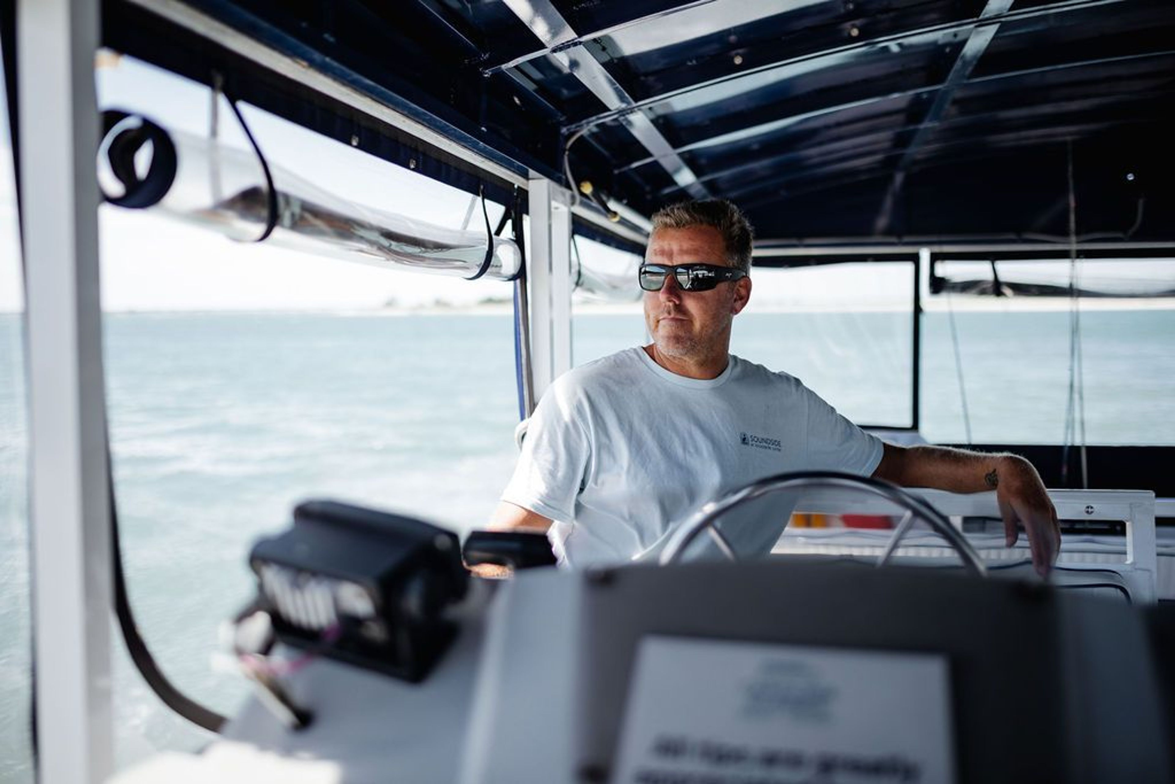 A man steering a boat with a view of the water in the background.