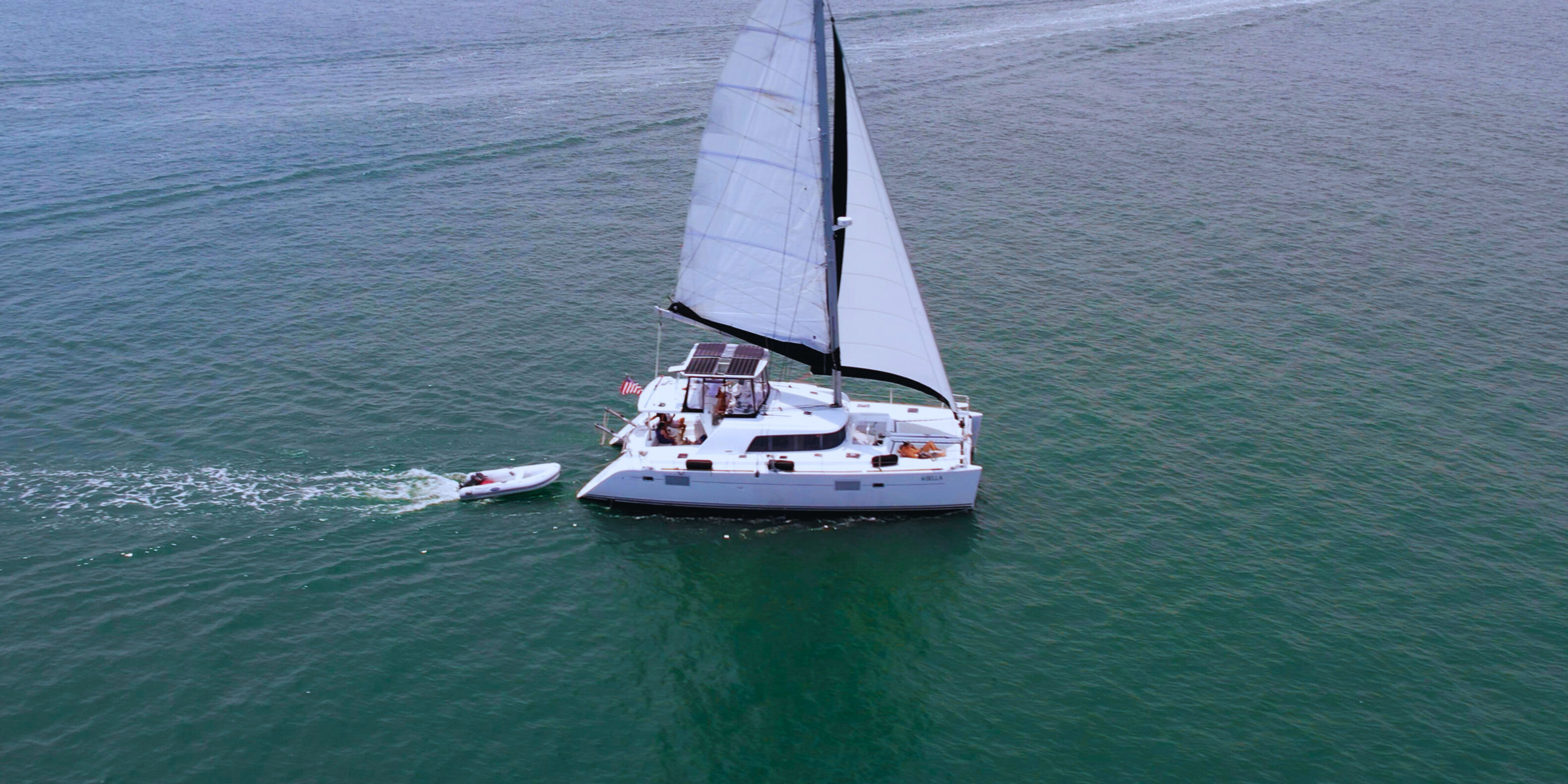 A sailboat with a dinghy in the water, surrounded by calm ocean waves.
