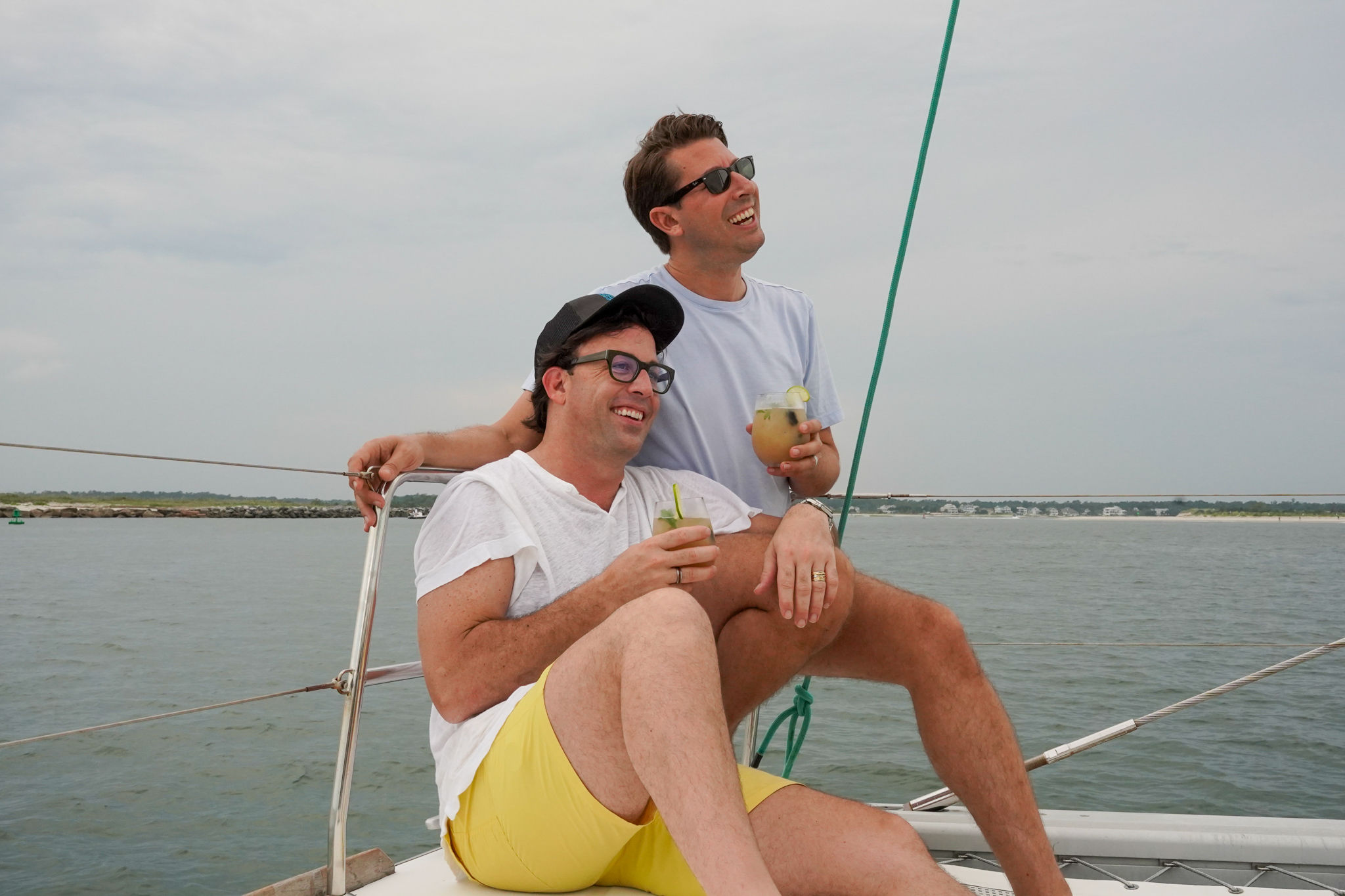Two men enjoying drinks on a sailboat with a scenic water background.