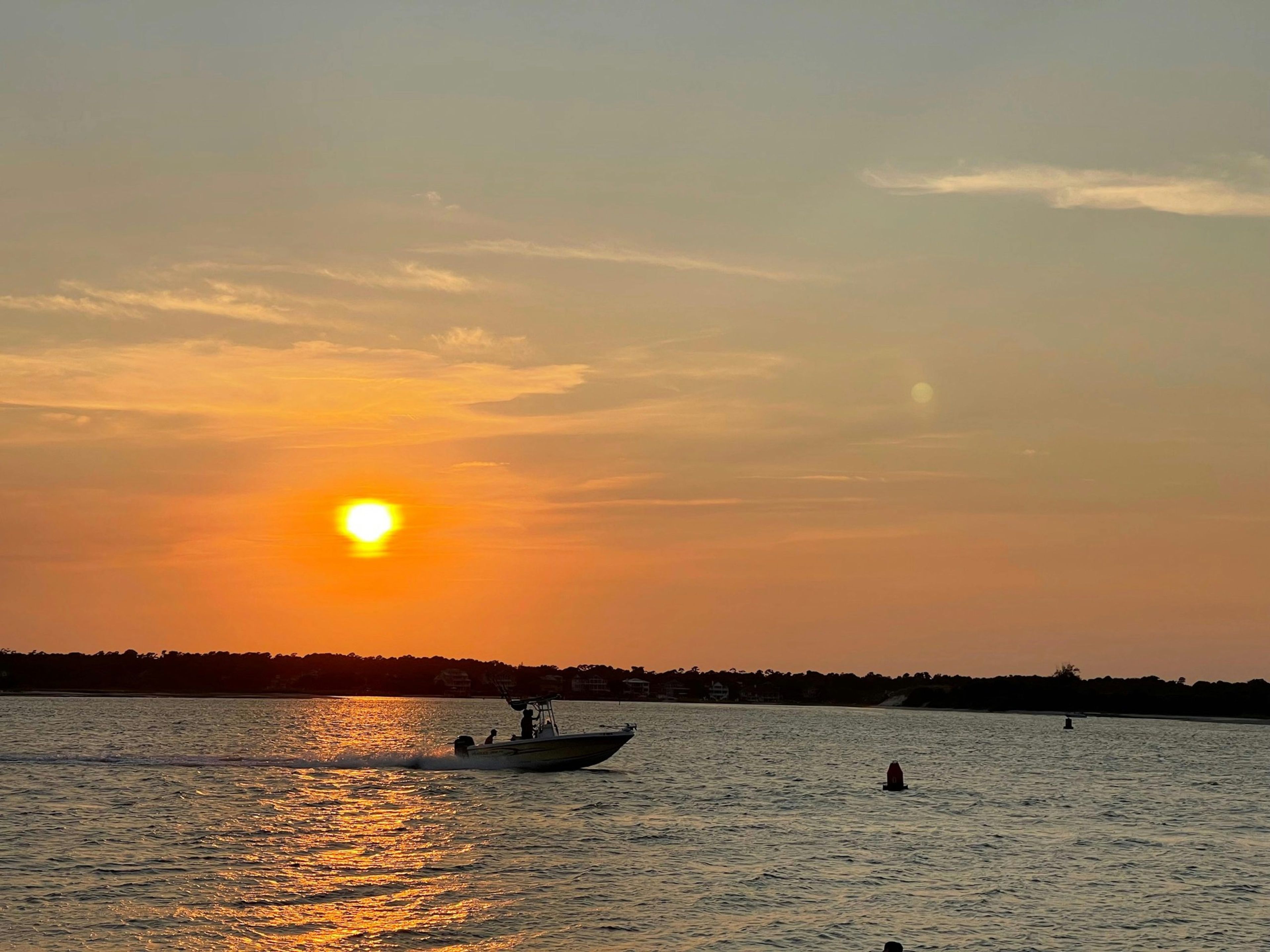 A sunset over water with a boat in the foreground and silhouettes of trees in the background.