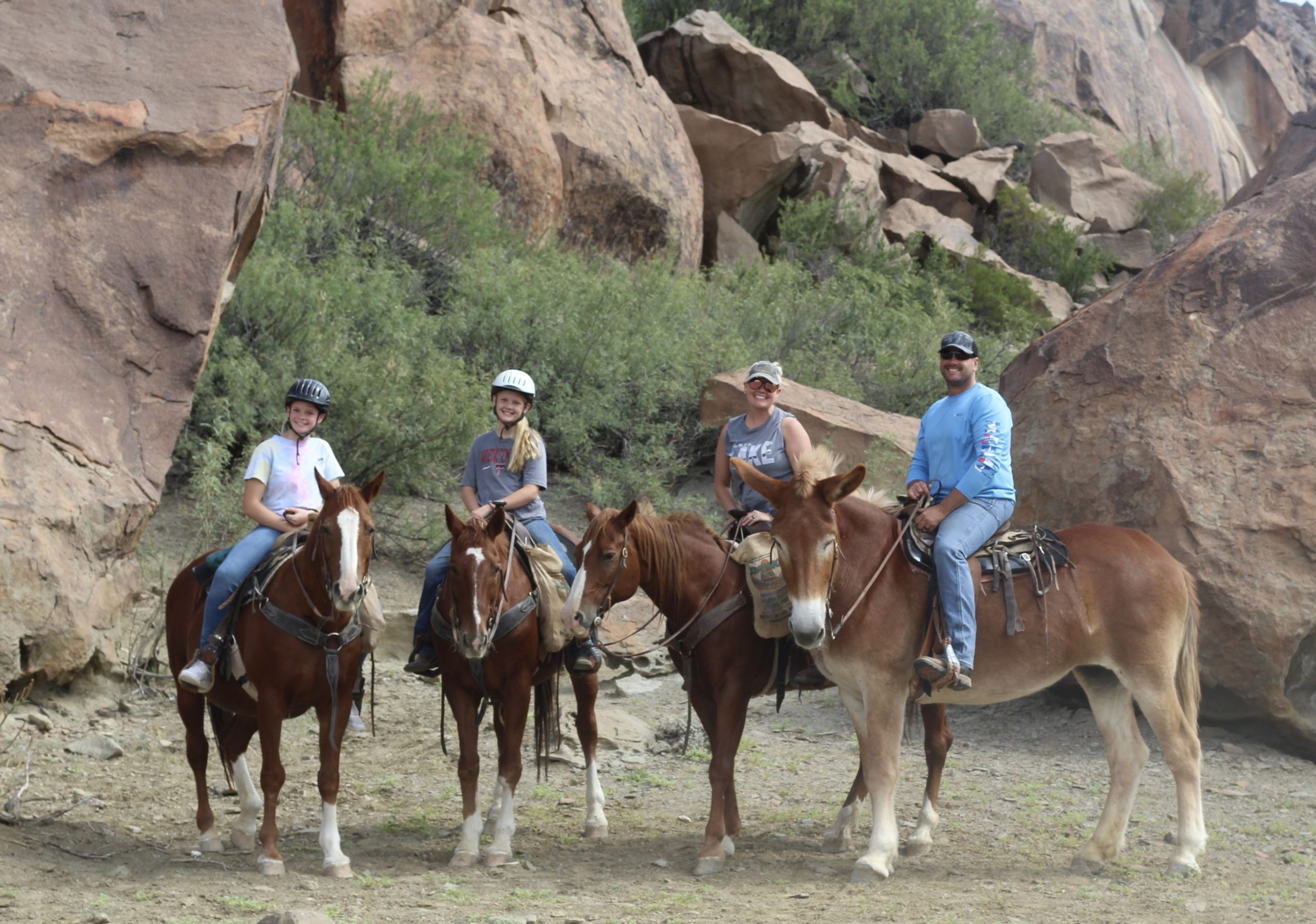 Four people on horseback in a rocky outdoor setting.