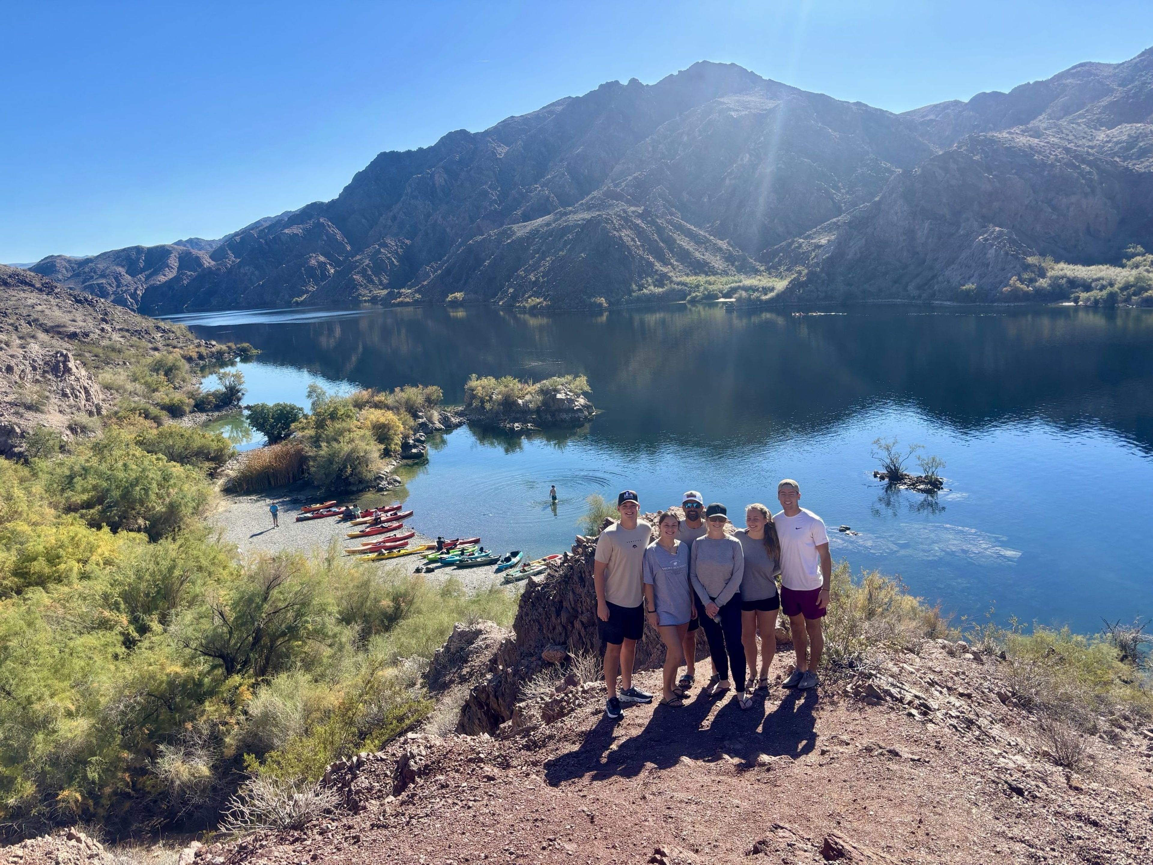 Group of five people posing by a river with mountains in the background