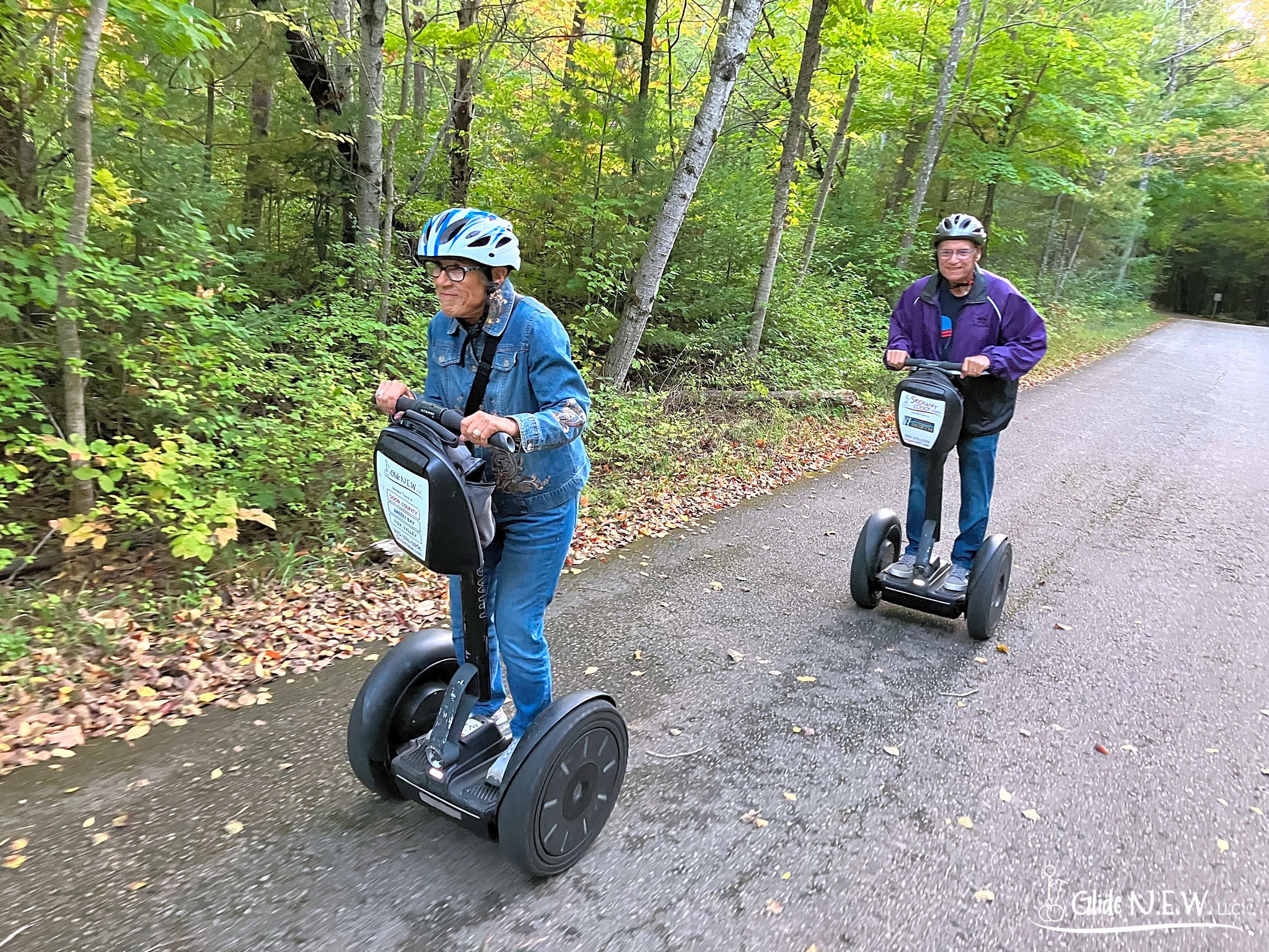 Two people riding Segways on a tree-lined path in autumn.