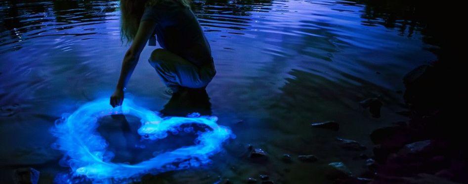 Woman drawing heart into the bioluminescent water.