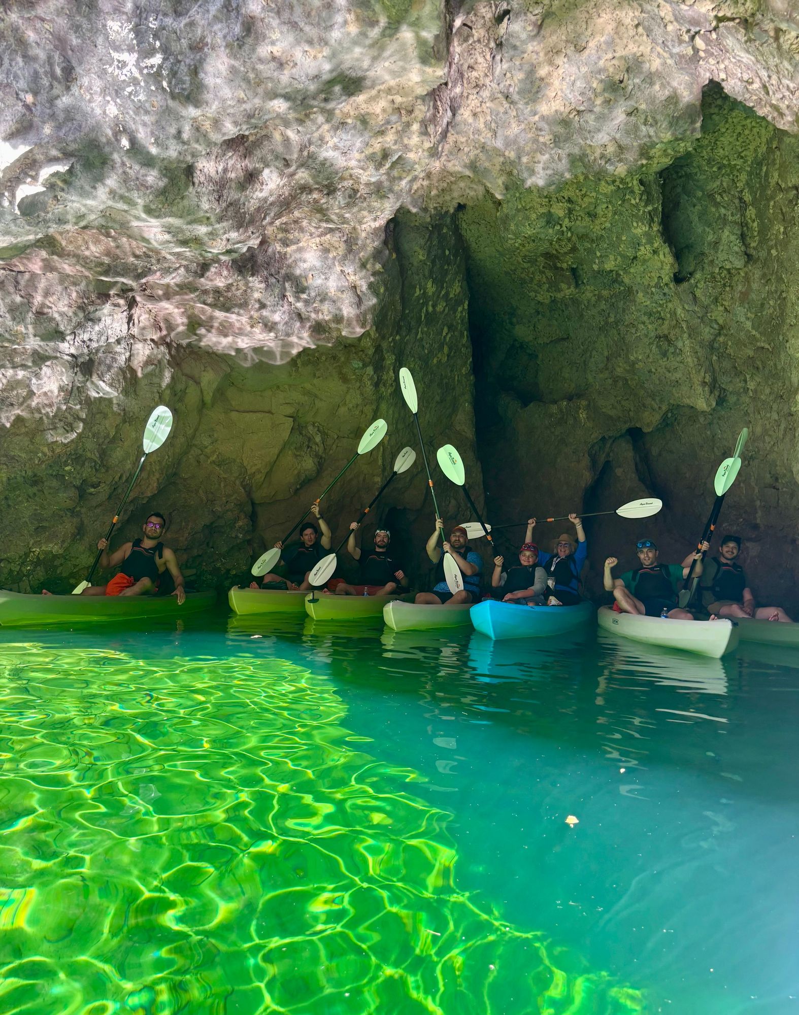 A private group of kayakers paddling into the vibrant, glowing waters of Emerald Cave, framed by dramatic canyon walls under bright daylight.