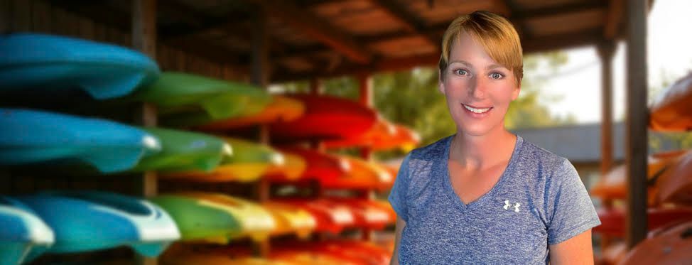 Astrid Jackson, founder of Venture Outdoors, standing in front of a colorful rack of kayaks at her Orlando outdoor adventure business