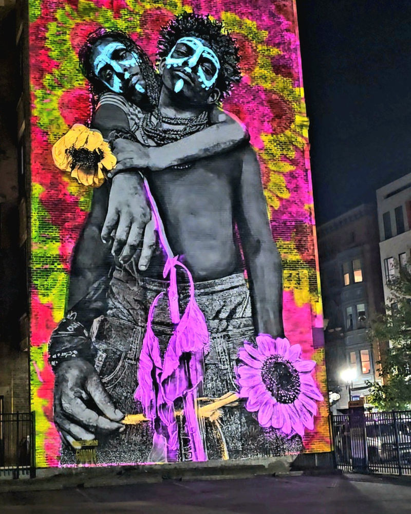 A mural by Gee Horton at Blink Cincinnati, featuring a powerful black-and-white portrait enhanced by a vibrant, colorful light projection designed by Greg D&rsquo;Amico.