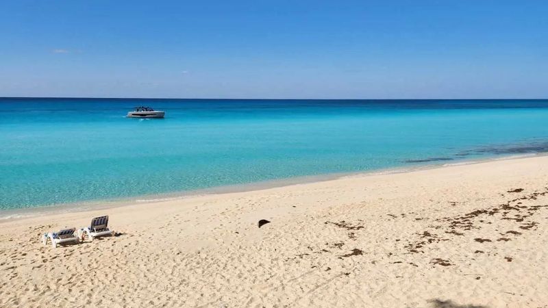 Bimini beach with lounge chairs, turquoise water, and boat. 