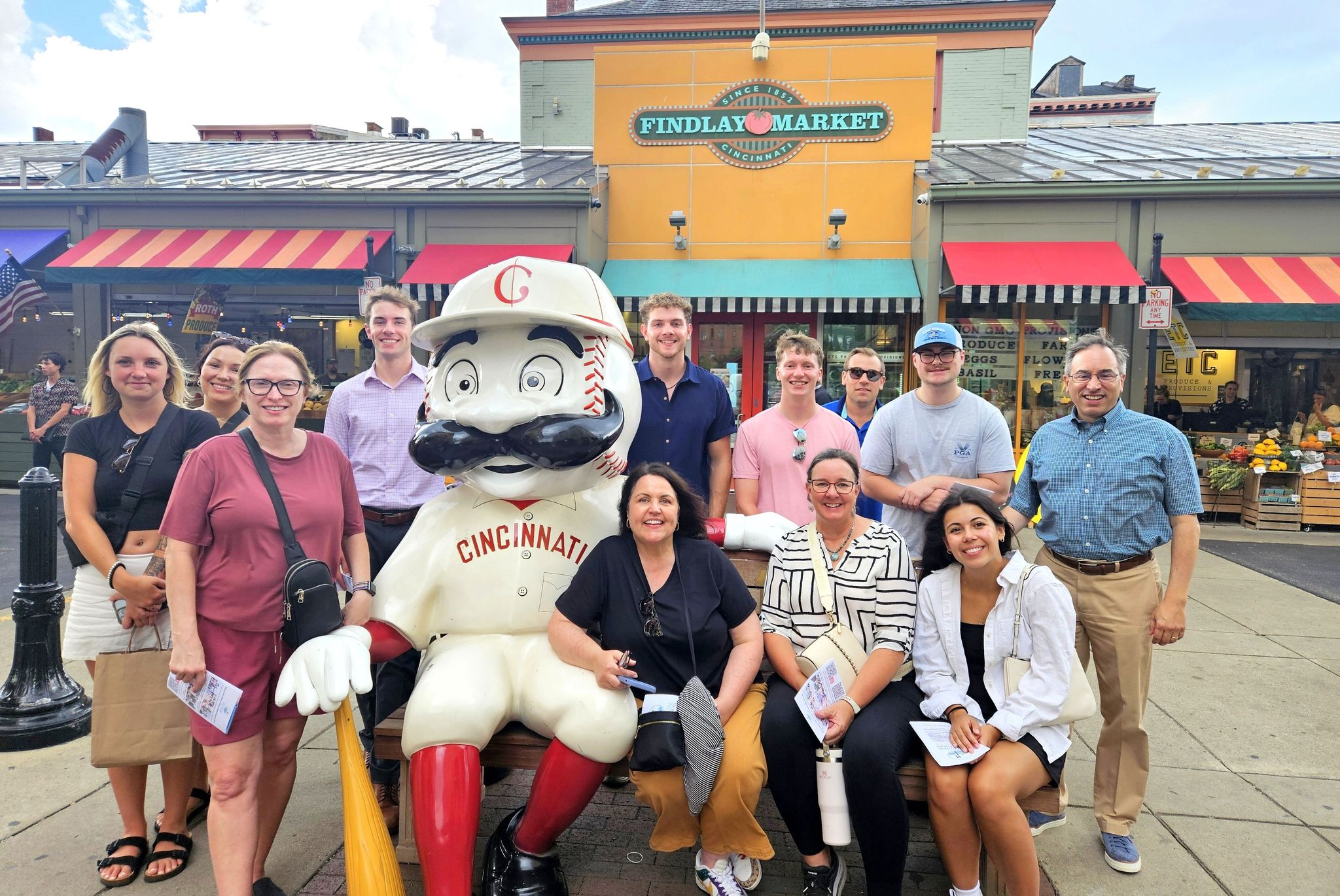A group of guests standing near Mr. Redlegs at Findlay Market for a Corporate team building food tour in downtown Cincinnati hosted by Riverside Food Tours