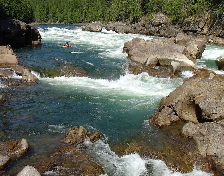 A view up river of a kayaker coming through the rapids