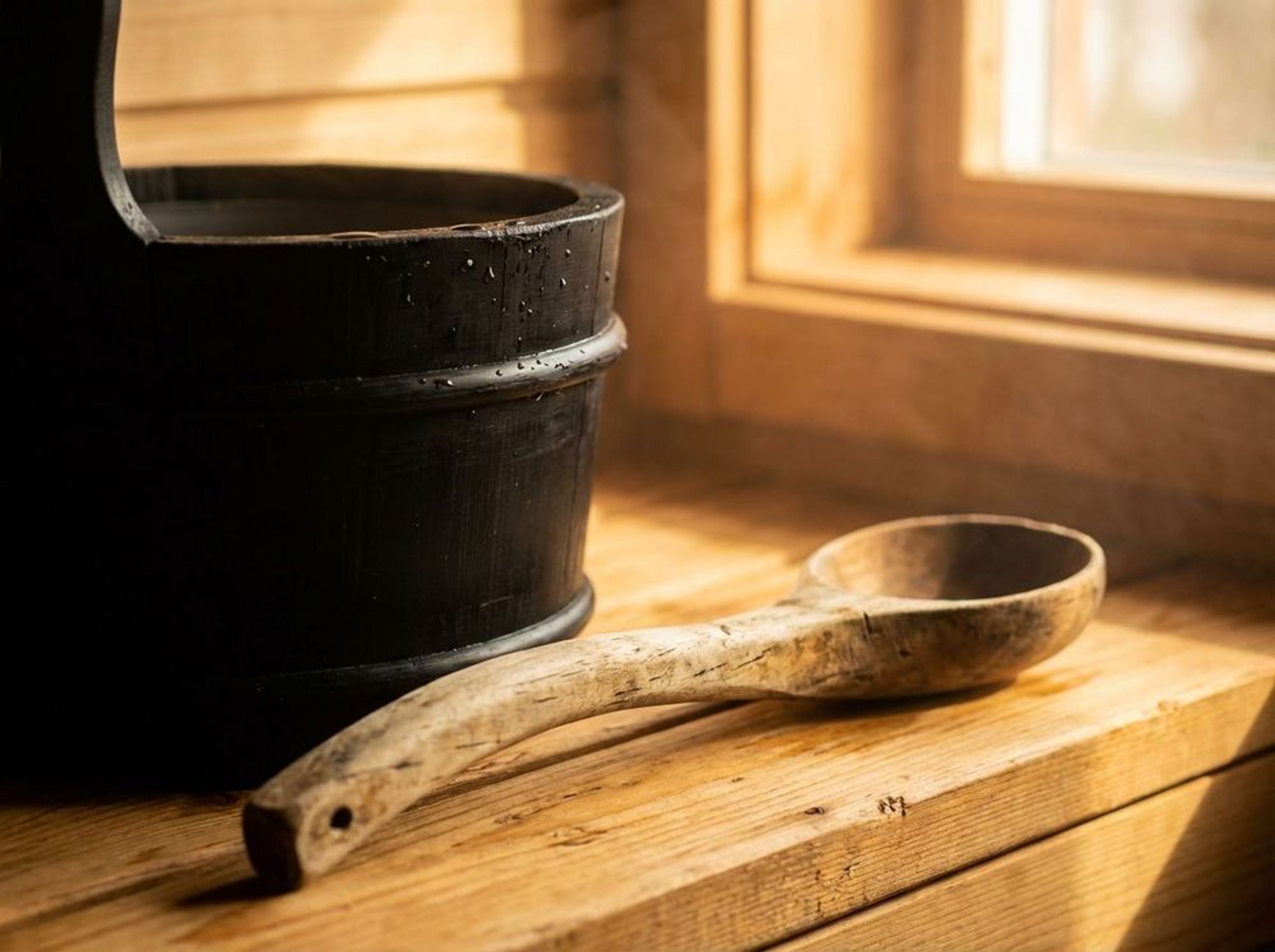 Traditional black sauna bucket and wooden ladle on cedar planks