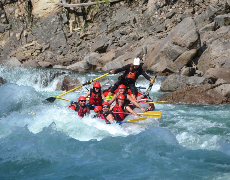 Family of rafters dipping into a big wave in bright blue water of the Clearwater River