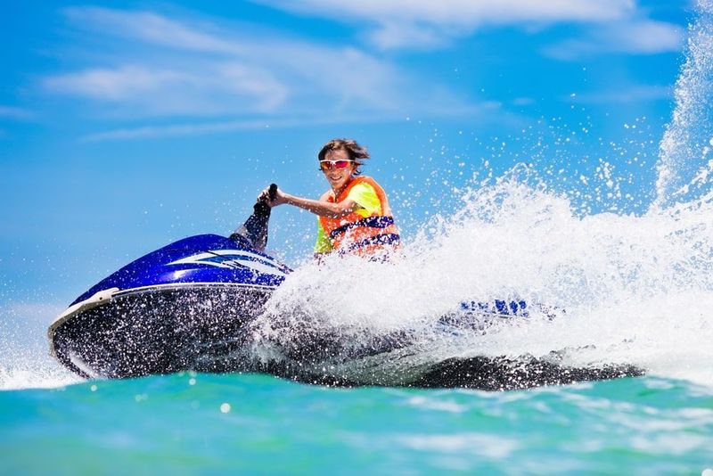 A person in a life vest enjoys jet skiing across vibrant blue water, creating a splash.