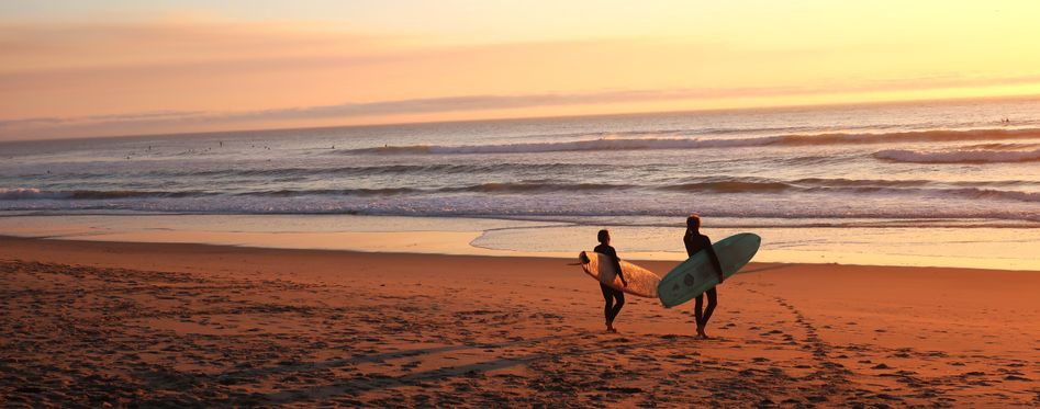 Two people on a beach with boards, about to paddle out