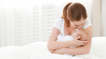 Uma mãe com uma blusa branca beijando um bebê que está em seus braços.