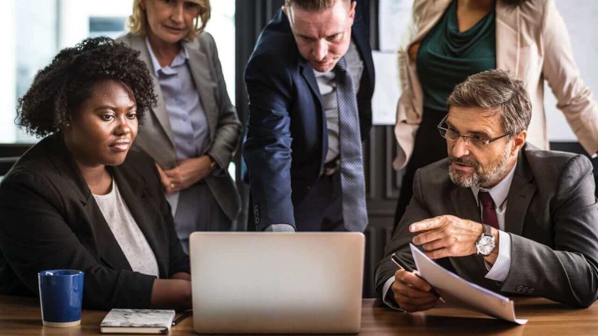 grupo de empresários, homens e mulheres, analisando um relatório no computador