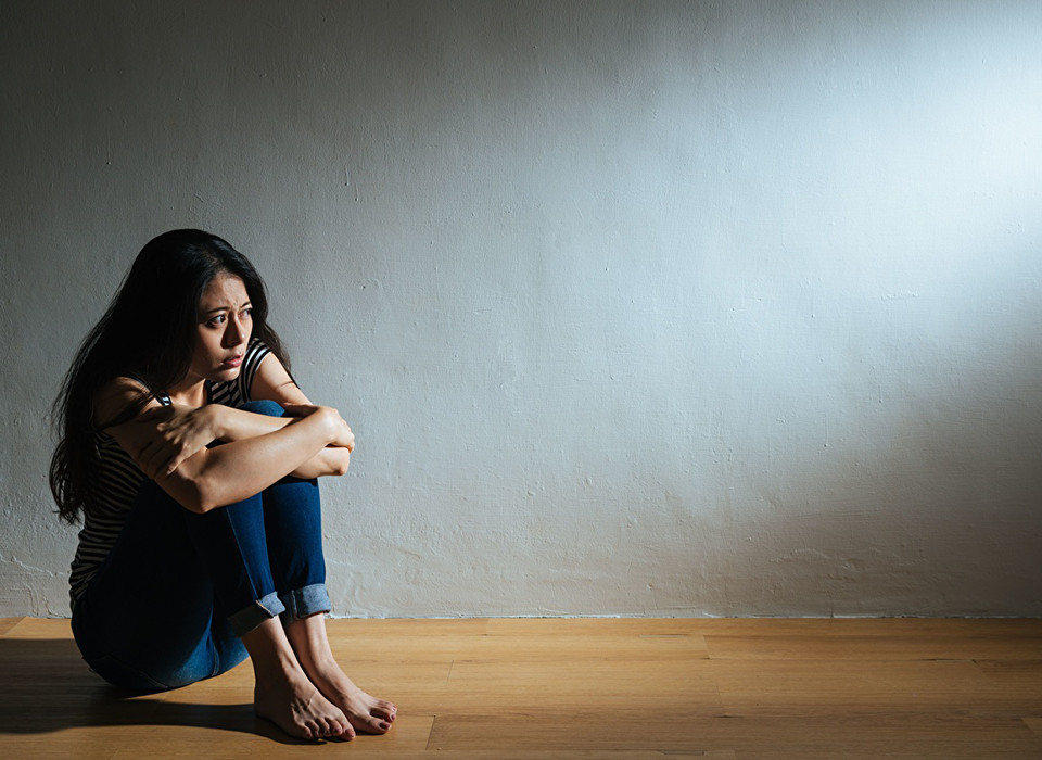 Imagem de uma mulher sentada no chão abraçando seus joelhos.