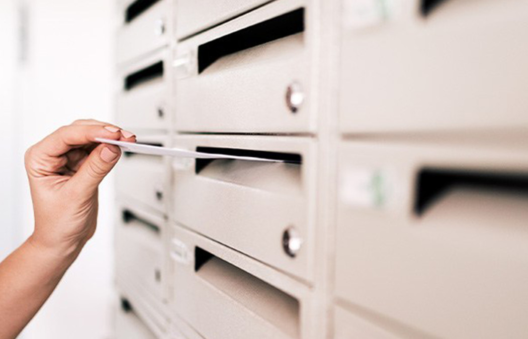 Imagem de uma mão retirando um envelope de um gaveta de correspondências.