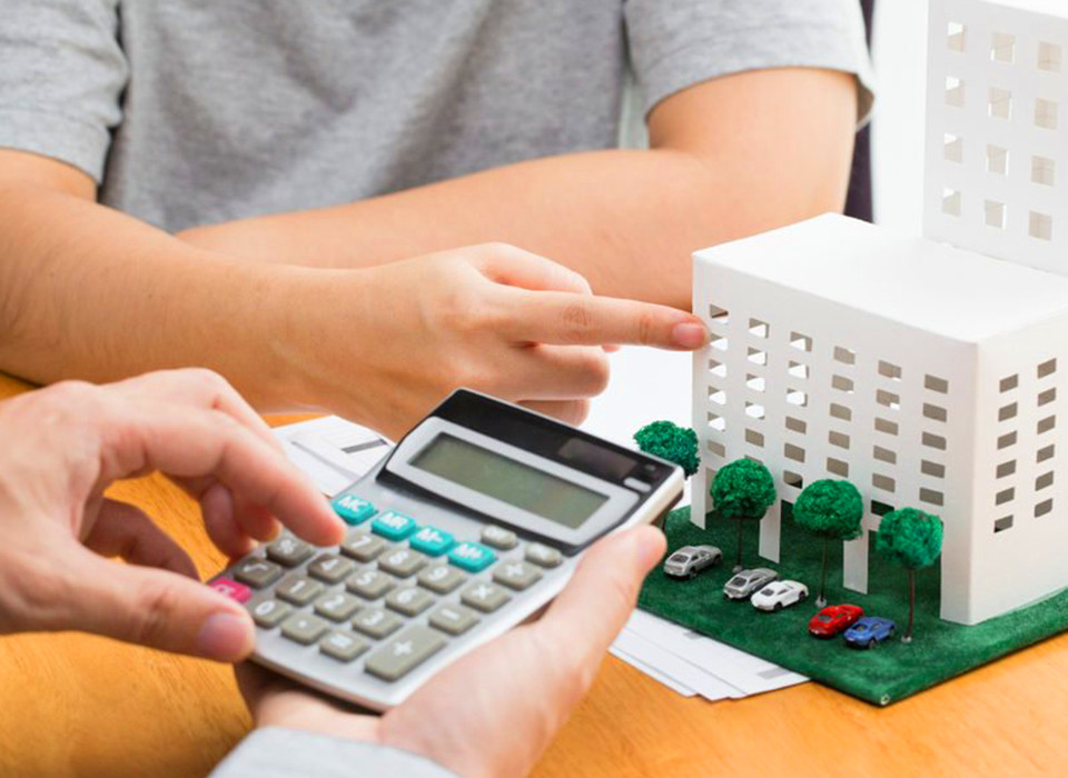 Imagem de uma pessoa fazendo uma conta na calculadora e outra analisando uma maquete de um prédio.