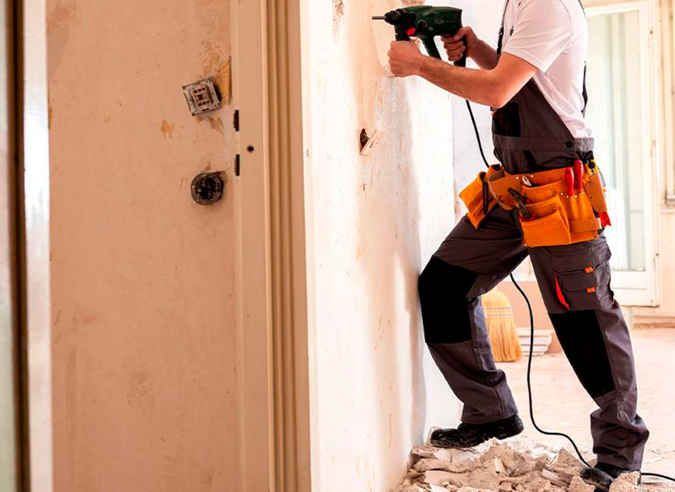 Imagem de um homem com uma furadeira realizando obras em um apartamento.