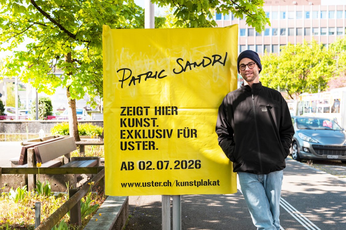 Der K&uuml;nstler Patric Sandri steht vor der gelb verh&uuml;llten Kunstplakat-Stelle