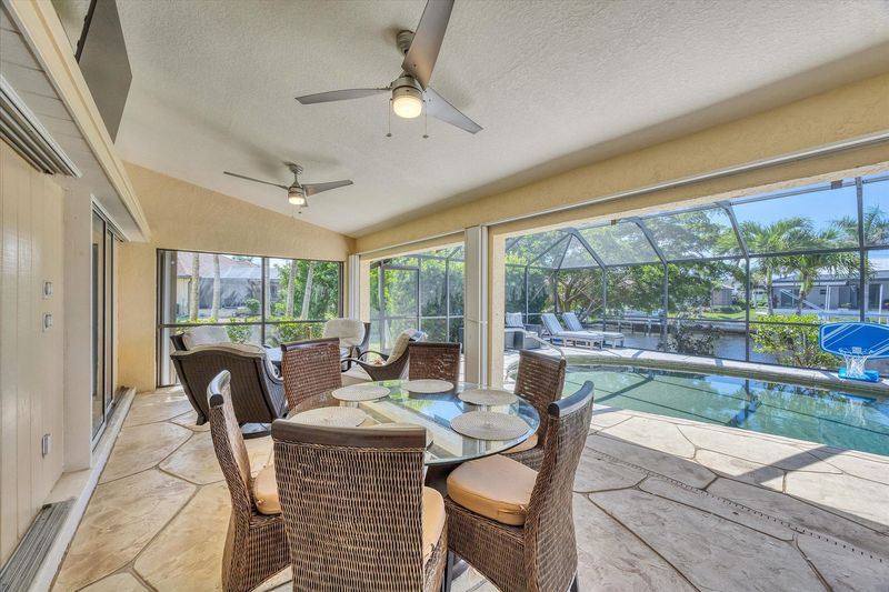 Amazing outdoor living space with dining table, sparkling pool, grill area with bar, and 55-inch Smart TV