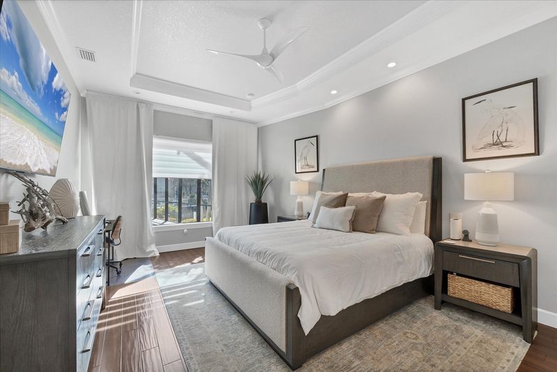 Primary bedroom features king bed, attached bathroom, desk & chair, 65-inch Smart TV, and beautiful view of pool and canal