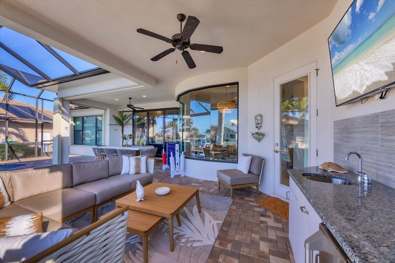 Gorgeous outdoor living space overlooking the sparkling private pool and canal beyond. Great for entertaining. This space features an outdoor kitchen, ample seating, grill, dining table that seats 8, and 50-inch Smart TV