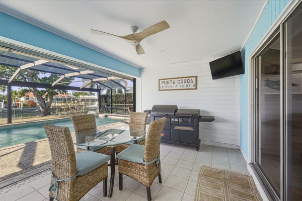 Large outdoor living space with dining table that seats 4, sun loungers, BBQ grill, sparkling pool, and 40-inch Smart TV