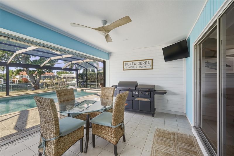 Large outdoor living space with dining table that seats 4, sun loungers, BBQ grill, sparkling pool, and 40-inch Smart TV