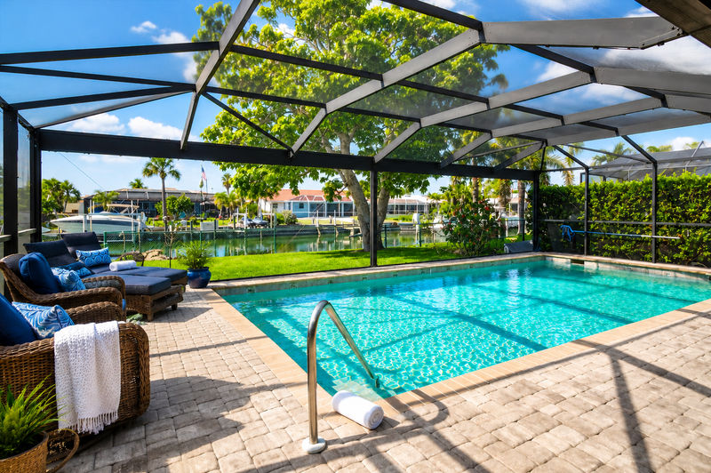 Large outdoor living space with dining table that seats 4, sun loungers, BBQ grill, sparkling pool, and 40-inch Smart TV