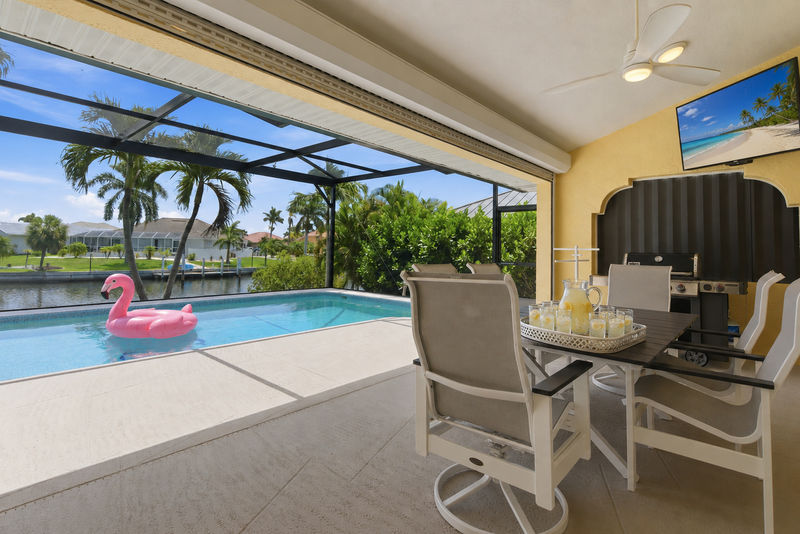 Large outdoor living space features a sparkling pool overlooking the canal, dining for 6, sun loungers, BBQ grill, and 50" Smart TV. Pool size: 29' x 13' x 6'D