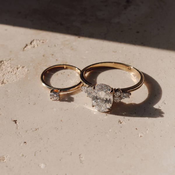 Two bespoke gold engagement rings with diamond settings resting on textured surface in warm natural light