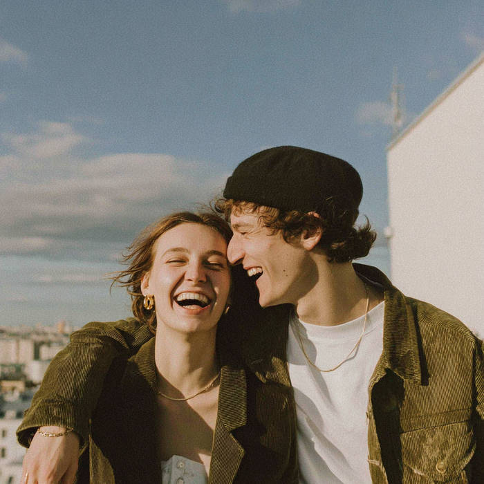 Laughing couple embracing on a rooftop, sunlit city skyline behind them under a blue sky