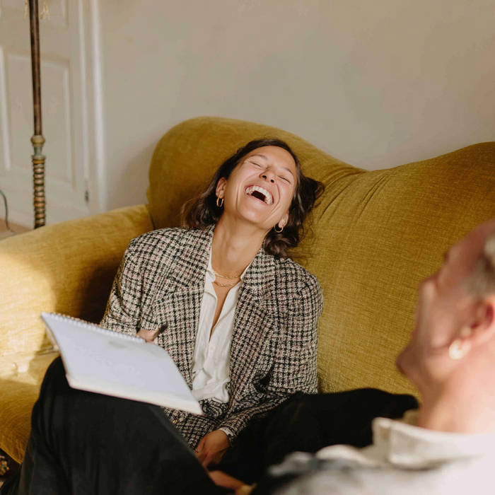 Woman laughing with a notepad during a relaxed consultation on a mustard sofa.