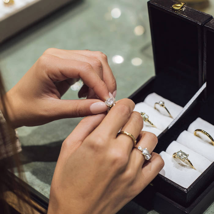 Hands trying on bespoke engagement rings from a jewellery box, comparing diamond styles on gold bands